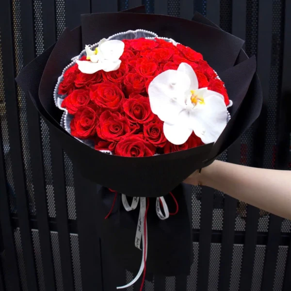 A bouquet of red roses and white orchids, wrapped in black paper, with ribbons.