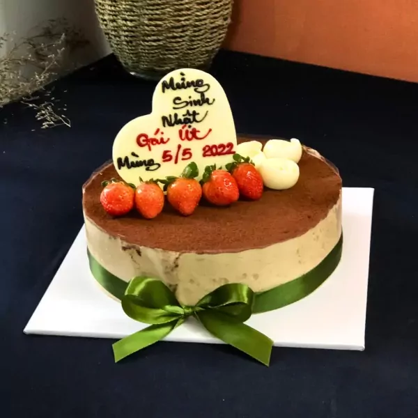 Tiramisu cake with strawberries, white chocolate hearts, and a green ribbon.