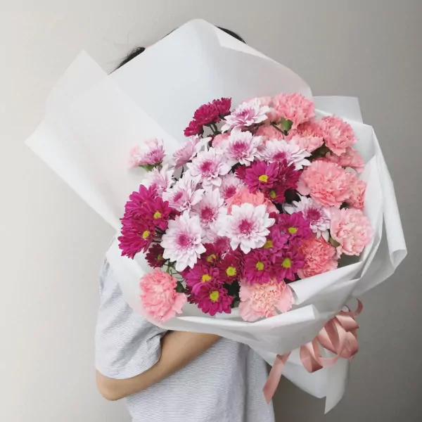 Bouquet of pink and purple chrysanthemums and carnations wrapped in white paper.