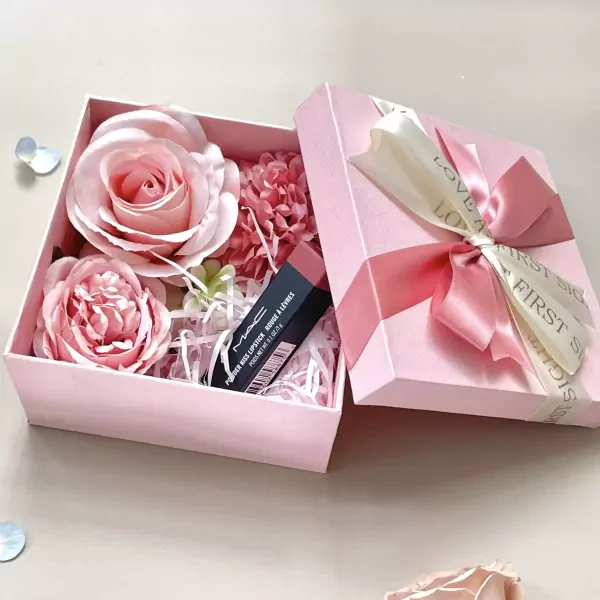 Pink gift box with faux roses and a MAC lipstick inside, tied with ribbons.