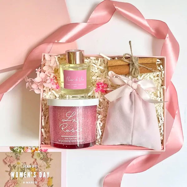 Pink gift box with candle, diffuser, and fabric pouch, adorned with ribbon and flowers.