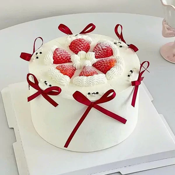 Christmas cake with strawberries, whipped cream, and red ribbons.