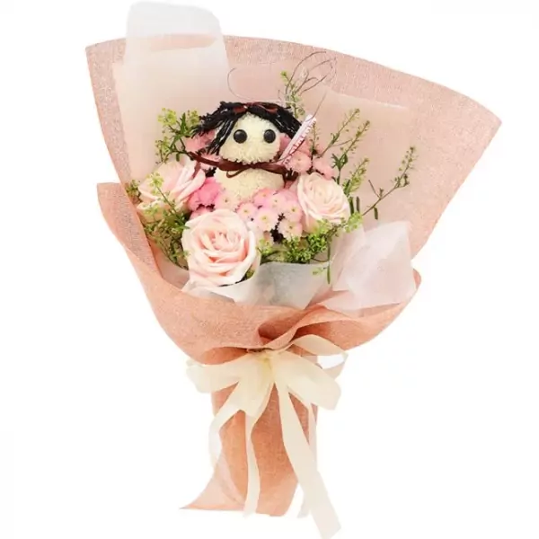 Pink roses, ping pong mums, and a doll in a bouquet wrapped in pink mesh.