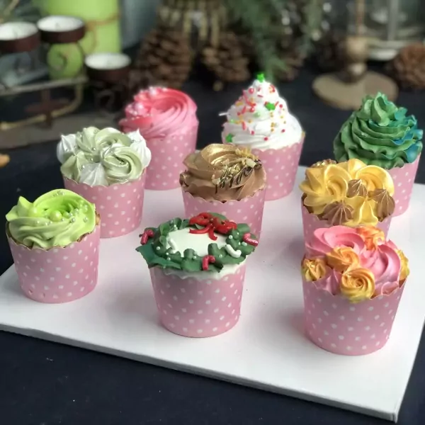 A collection of nine colorful cupcakes with various frosting designs, presented in pink polka-dot wrappers.