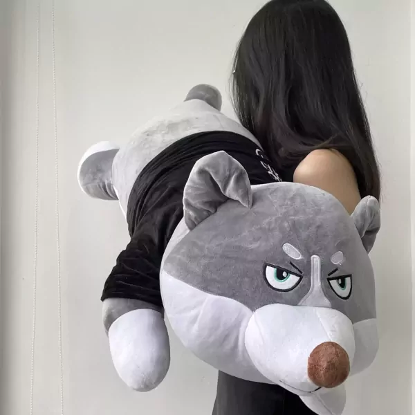Giant grey plush puppy with a grumpy expression, wearing a black shirt, held by a person.