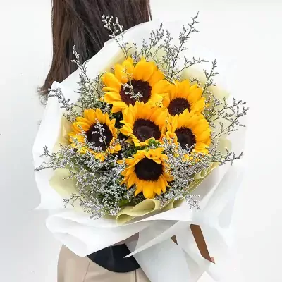 Bouquet of six sunflowers and purple statice, wrapped in white and pale yellow paper.