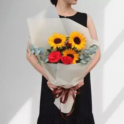 Bouquet of sunflowers and red roses with eucalyptus, wrapped in light paper and tied with a brown ribbon.