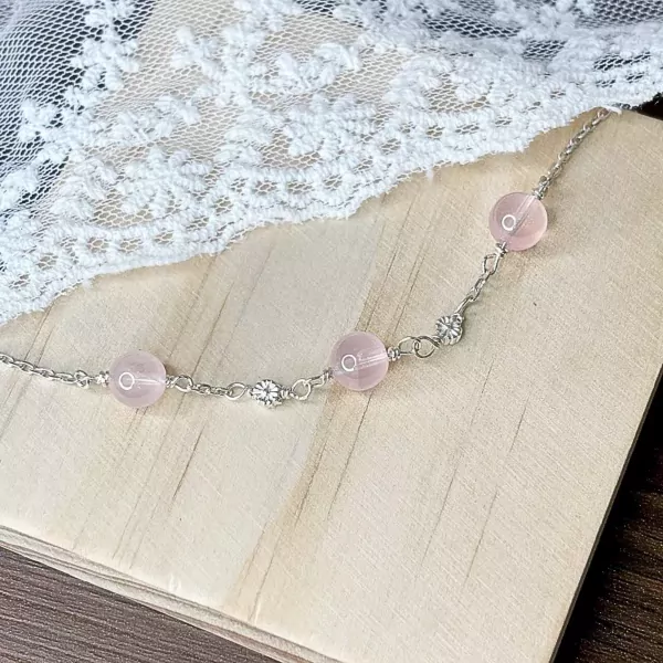 Silver chain bracelet with rose quartz beads and small floral charms.