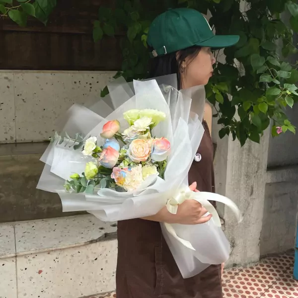 Woman holding a rainbow-colored bouquet of roses, carnations, and hydrangeas.