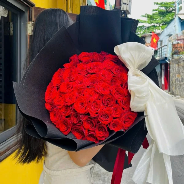 Bouquet of 50 red roses with a white bow on black wrapping.
