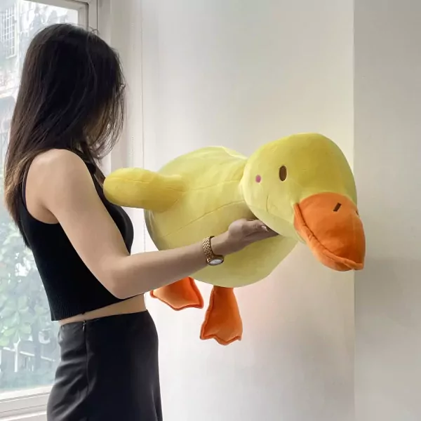 A woman holds a large, soft yellow duck plush toy with orange feet and beak.