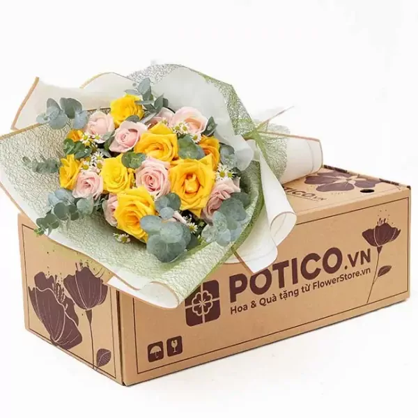 Yellow and pink roses, eucalyptus, and baby's breath in a bouquet on a cardboard box.