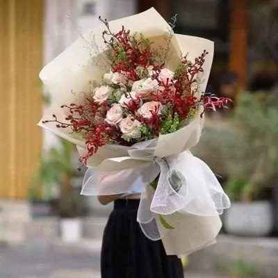 Bouquet of pink roses, red cymbidium orchids, and greenery, wrapped in cream paper and white tulle.