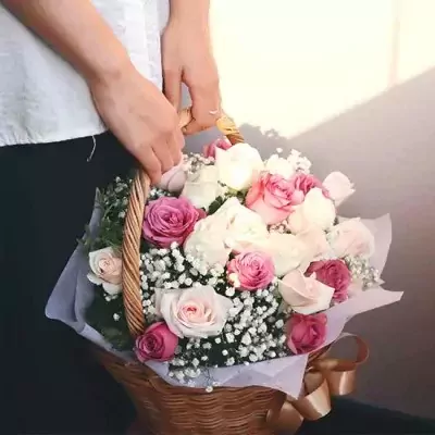 Basket of pink and white roses with baby's breath, held by two hands.