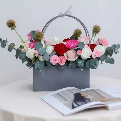 Floral arrangement in a gray box with white and pink roses, red carnations, and eucalyptus.