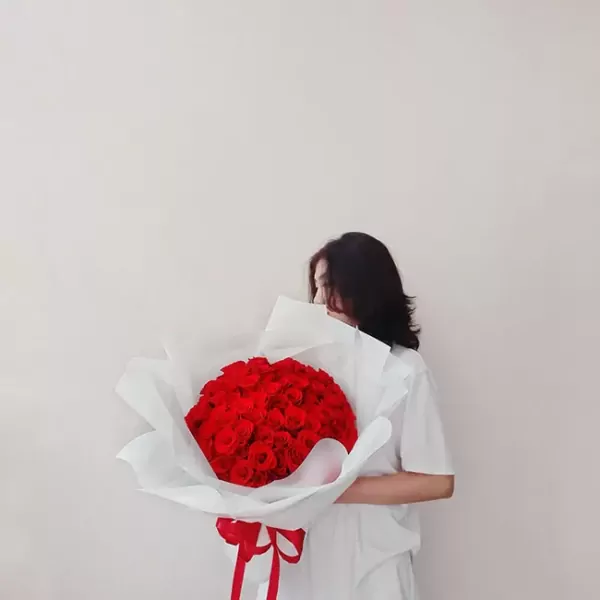 Woman in white holding a large bouquet of red roses.