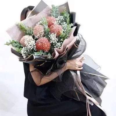 A bouquet of brown peonies with baby's breath and eucalyptus, wrapped in black and pink paper.