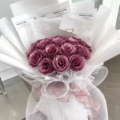 Amethyst pink bouquet of glittery roses, wrapped in white paper and netting, with decorative ribbons.
