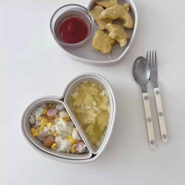 Heart-shaped lunchbox with rice, corn, sausage, soup, chicken nuggets, and ketchup.