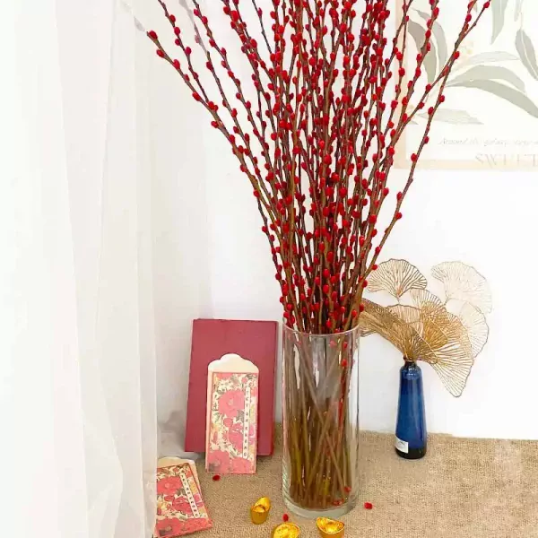 Red catkins in a tall glass vase with red envelopes and gold ingots.