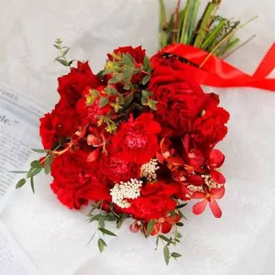 A lush bouquet of red roses, carnations, and orchids tied with a red ribbon.