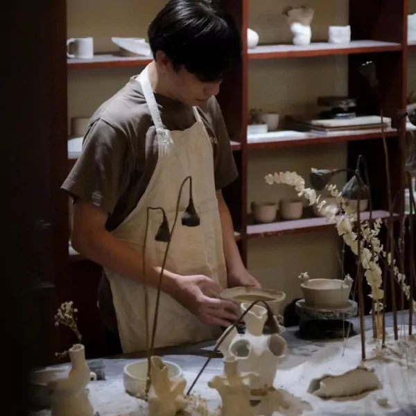 Potter working at a clay pottery workshop with shelves of ceramics.