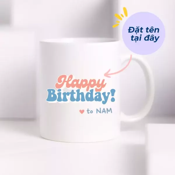 White ceramic mug with "Happy Birthday! to NAM" in coral and blue text.