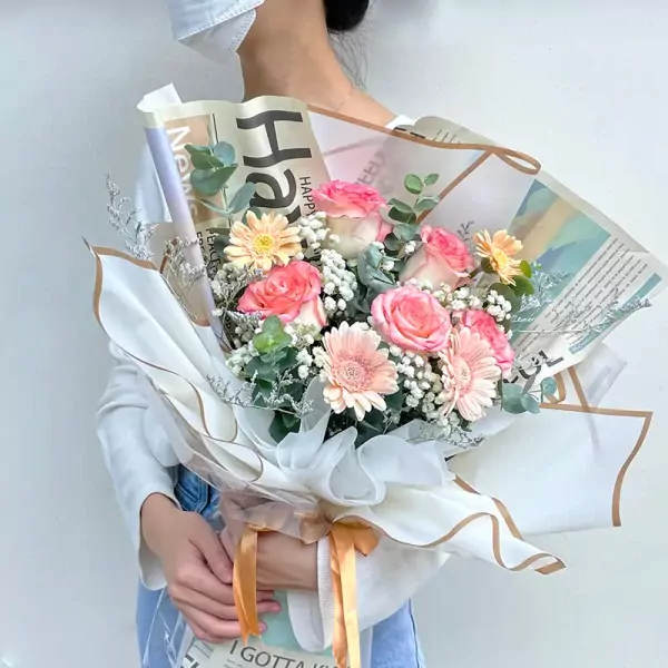 A bouquet of pink roses and orange gerbera daisies wrapped in newspaper and white paper.
