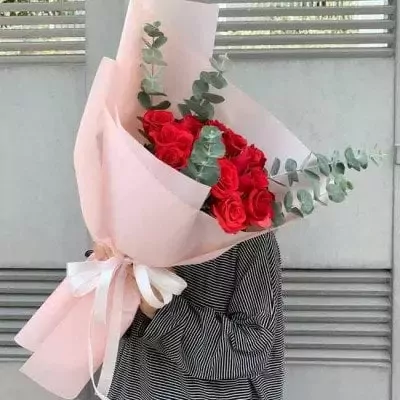 Bouquet of red roses and eucalyptus, wrapped in pink paper with a white ribbon.