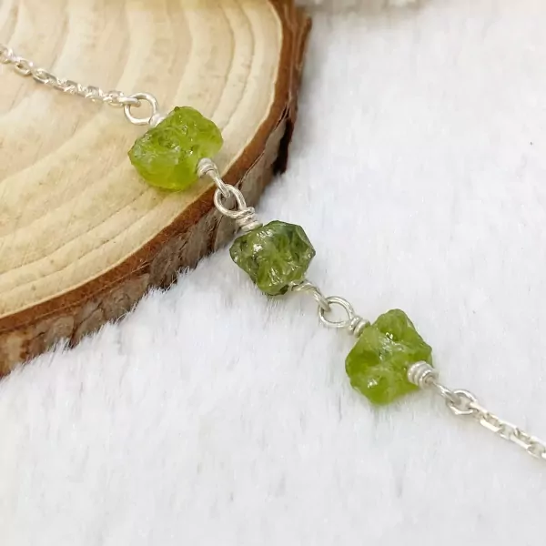 Silver bracelet with rough green stones on a wooden surface.