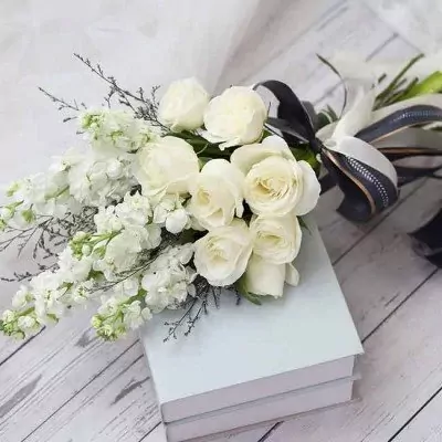 White roses and stock flowers bouquet on a stack of light blue books with a dark ribbon.