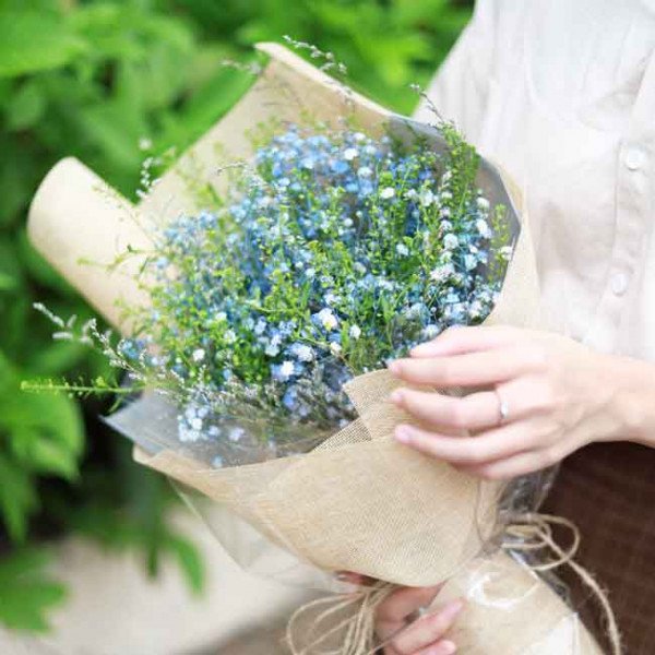 A bouquet of blue baby's breath flowers wrapped in burlap and paper.