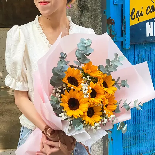 A person holds a bouquet of sunflowers, baby's breath, and eucalyptus.