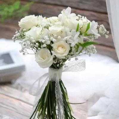 White roses and baby's breath bouquet with lace ribbon, ideal for weddings.
