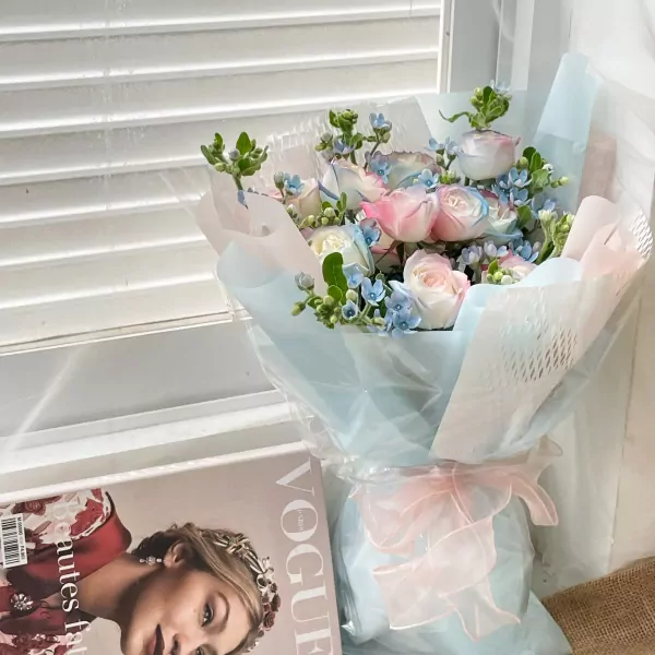 A bouquet of pink and blue roses with delicate baby's breath, wrapped in pale blue paper with a pink ribbon.