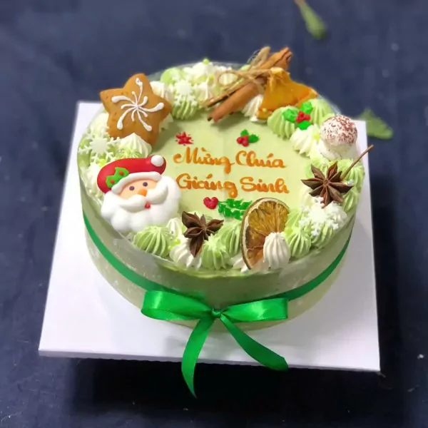 Green matcha mousse cake with Santa Claus, star cookie, orange slice, and cinnamon sticks.