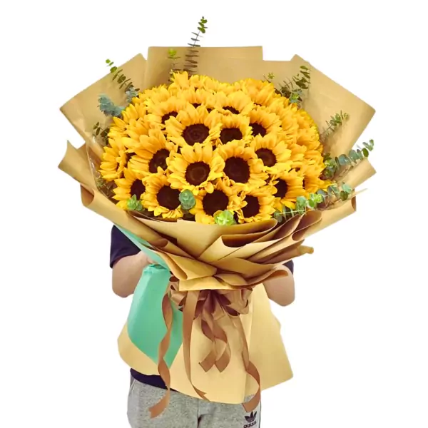 A bouquet of 36 sunflowers wrapped in brown and green paper, held by a person.