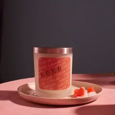 Candle with "XOXO" on the label, on a pink saucer with heart-shaped candies.