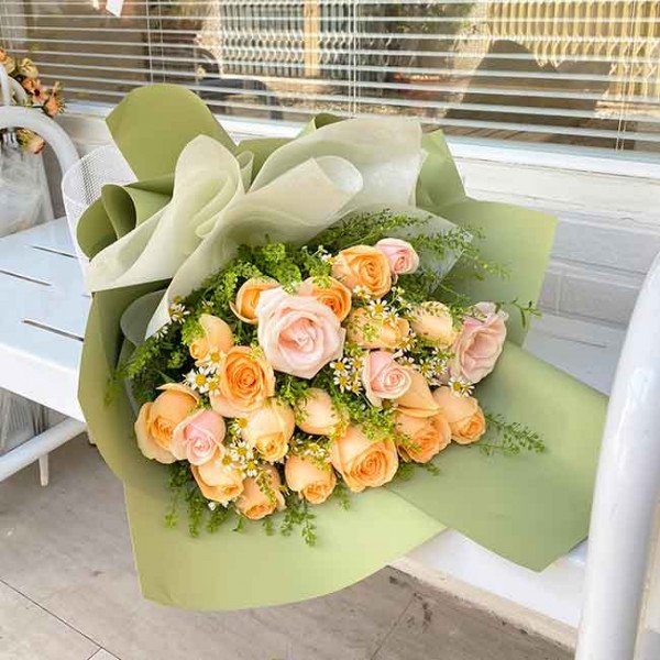 Bouquet of pink and peach roses with white accent flowers, wrapped in green paper.