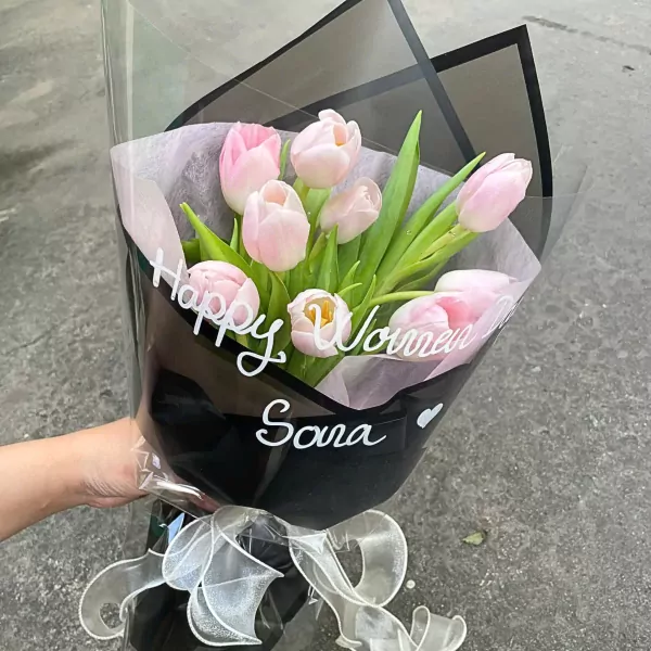 Pink tulips in a black wrapper with "Happy Women's Day Sara" written in white.