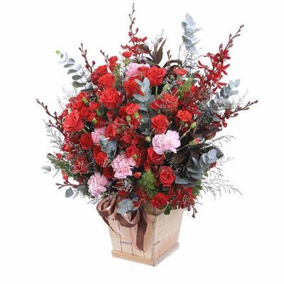 Red roses and pink carnations in a wooden basket with a brown ribbon.