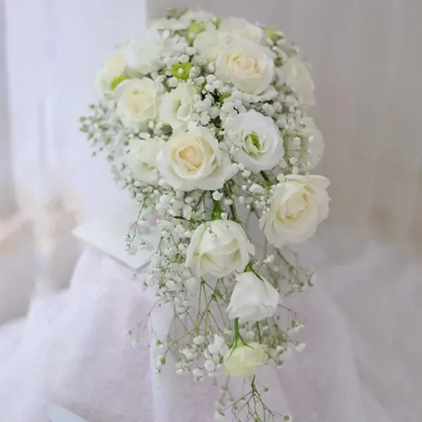 Cascading bouquet of white roses and baby's breath on a white cloth.