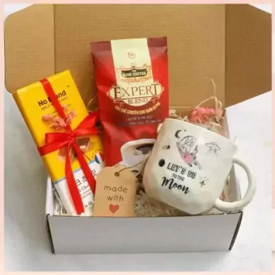 Gift box with coffee, yellow item, mug with cartoon drawing, and tag.