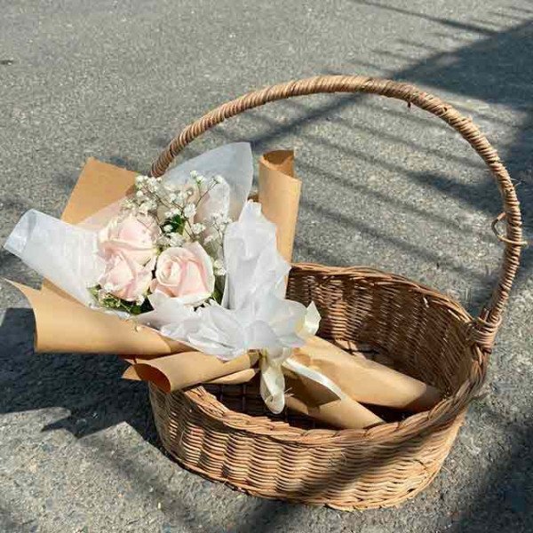 A floral arrangement in a basket with pink roses and baby's breath.