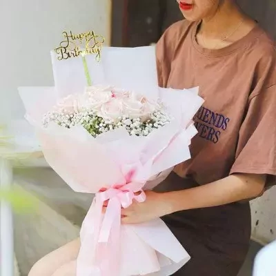 Woman holding a pink and white rose bouquet with a 'Happy Birthday' topper.