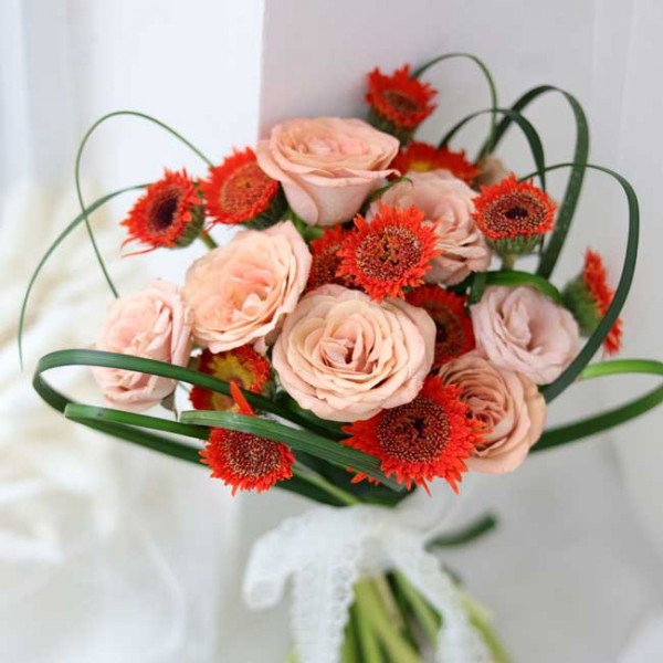 A bouquet of peach roses and orange gerbera daisies with green foliage.