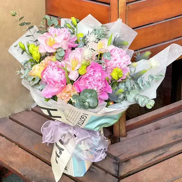A bouquet of pink peonies, tulips, and carnations wrapped in newspaper and ribbon.
