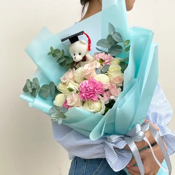 Graduation bouquet with teddy bear in cap, white and pink roses, carnations, and chrysanthemums.