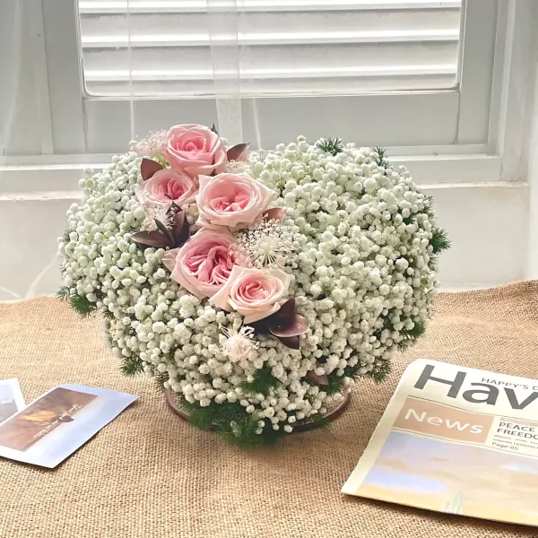 Heart-shaped arrangement of pink roses and baby's breath on a burlap surface.