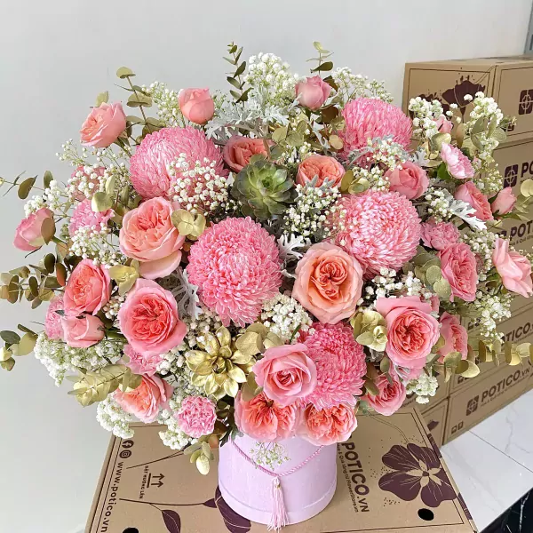 Pink peonies, roses, and carnations in a round pink box with gold accents.